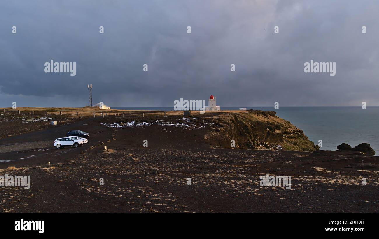 View over the top of Dyrhólaey peninsula on the south coast of Iceland with parking cars and lighthouse in winter season in the evening light. Stock Photo