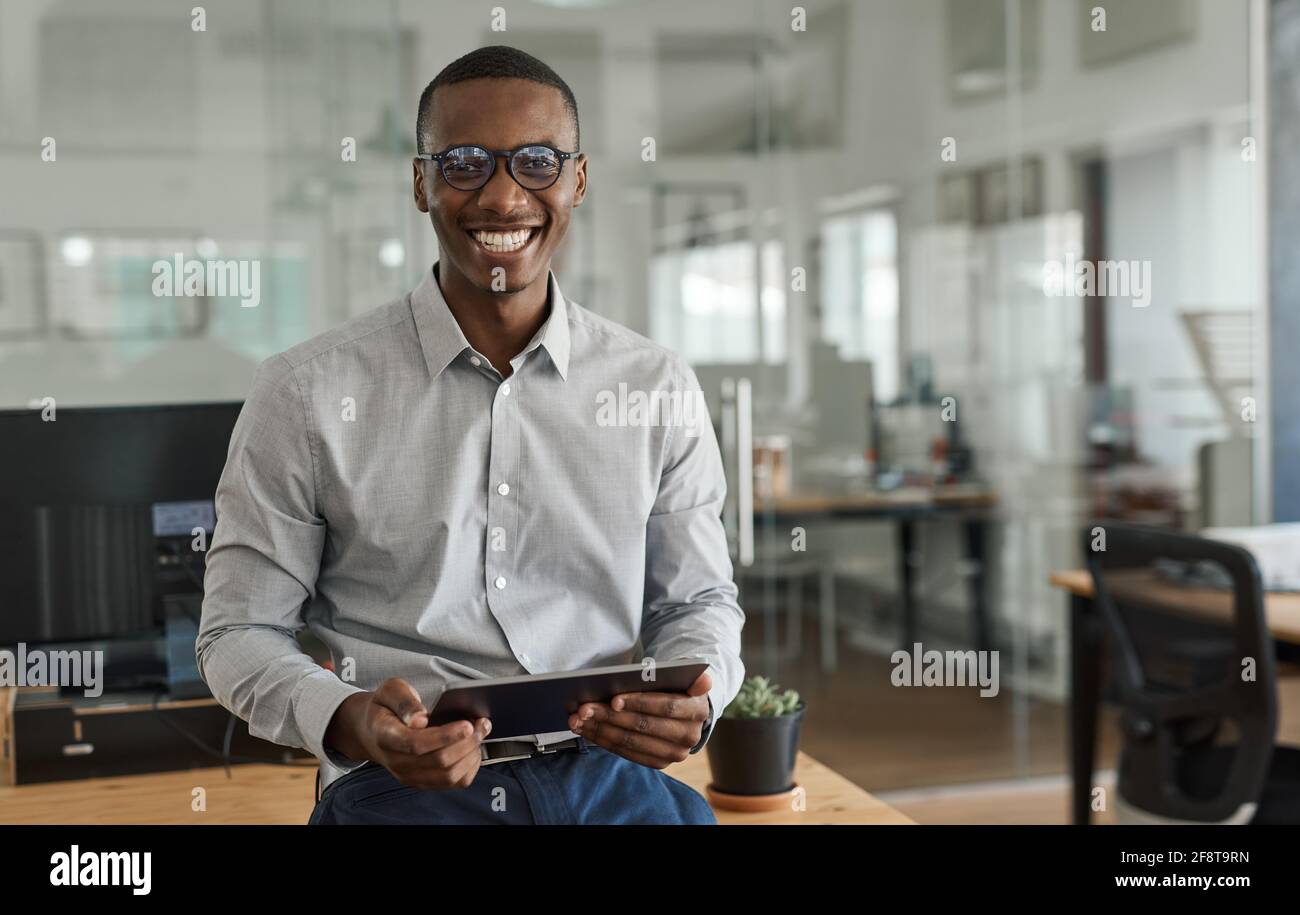Smiling African businessman using a tablet at his office desk Stock Photo