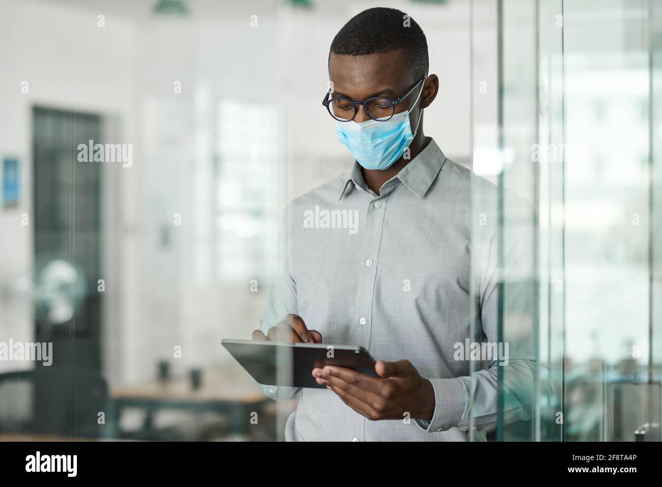 African businessman in a face mask using a tablet at work Stock Photo