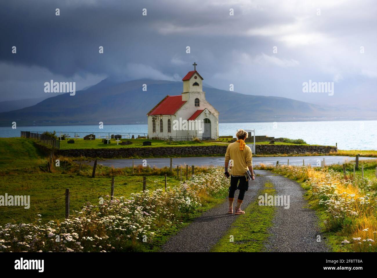 Young man with a skateboard looking at a church with a cemetery in Iceland Stock Photo