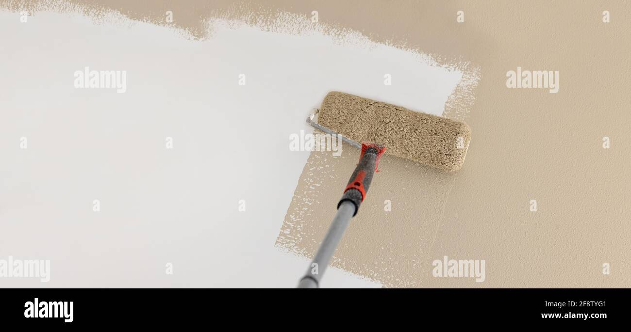 painting wall in mocha beige color with paint roller. banner copy space Stock Photo