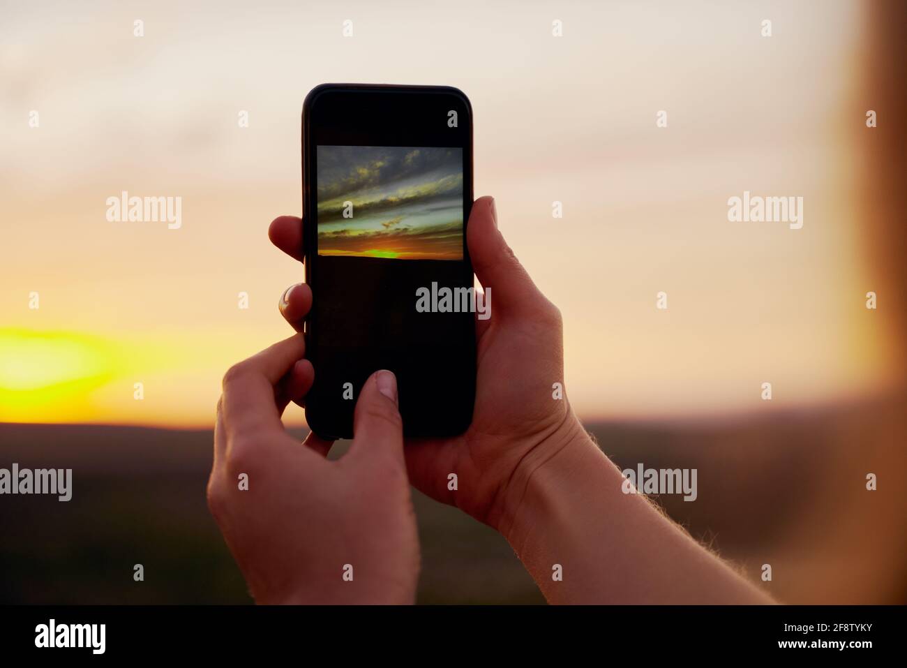Closeup of hands of young male hiker clicking beautiful morning sunrise on smartphone Stock Photo