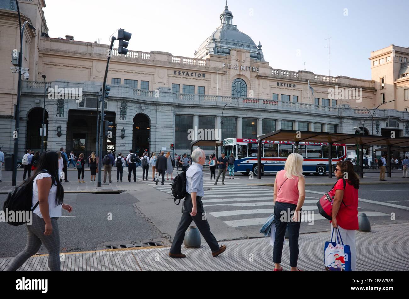 Buenos Aires, Argentina - January, 2020: A lot of people crossing road at pedestrian crossing near bus stop in front of main entrance to the building Stock Photo