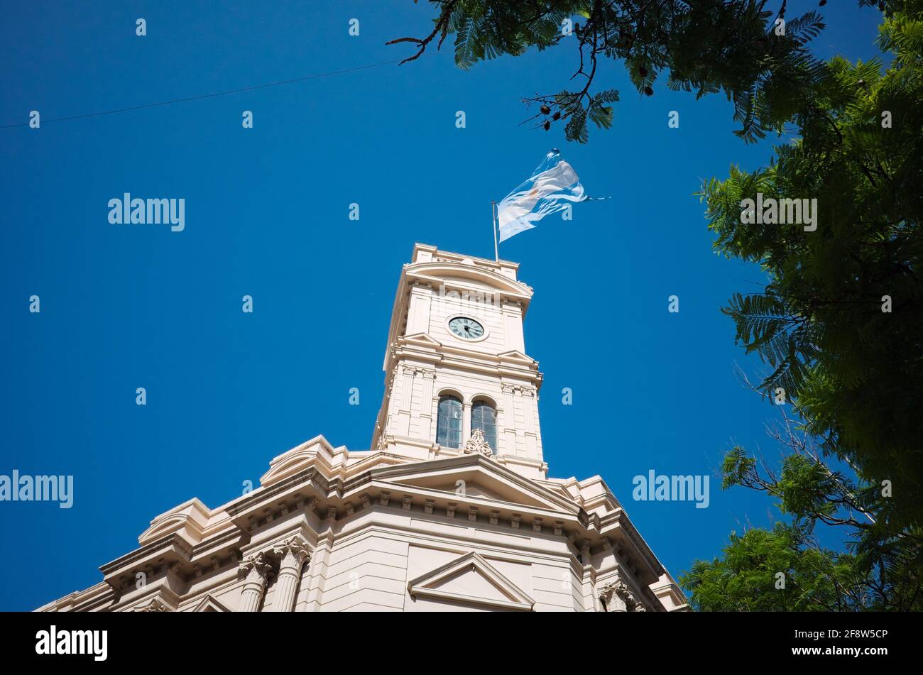 Flag of Argentina waving over clock tower against blue sky on the building of Legislature of the Province of Cordoba. Historic building in the center Stock Photo