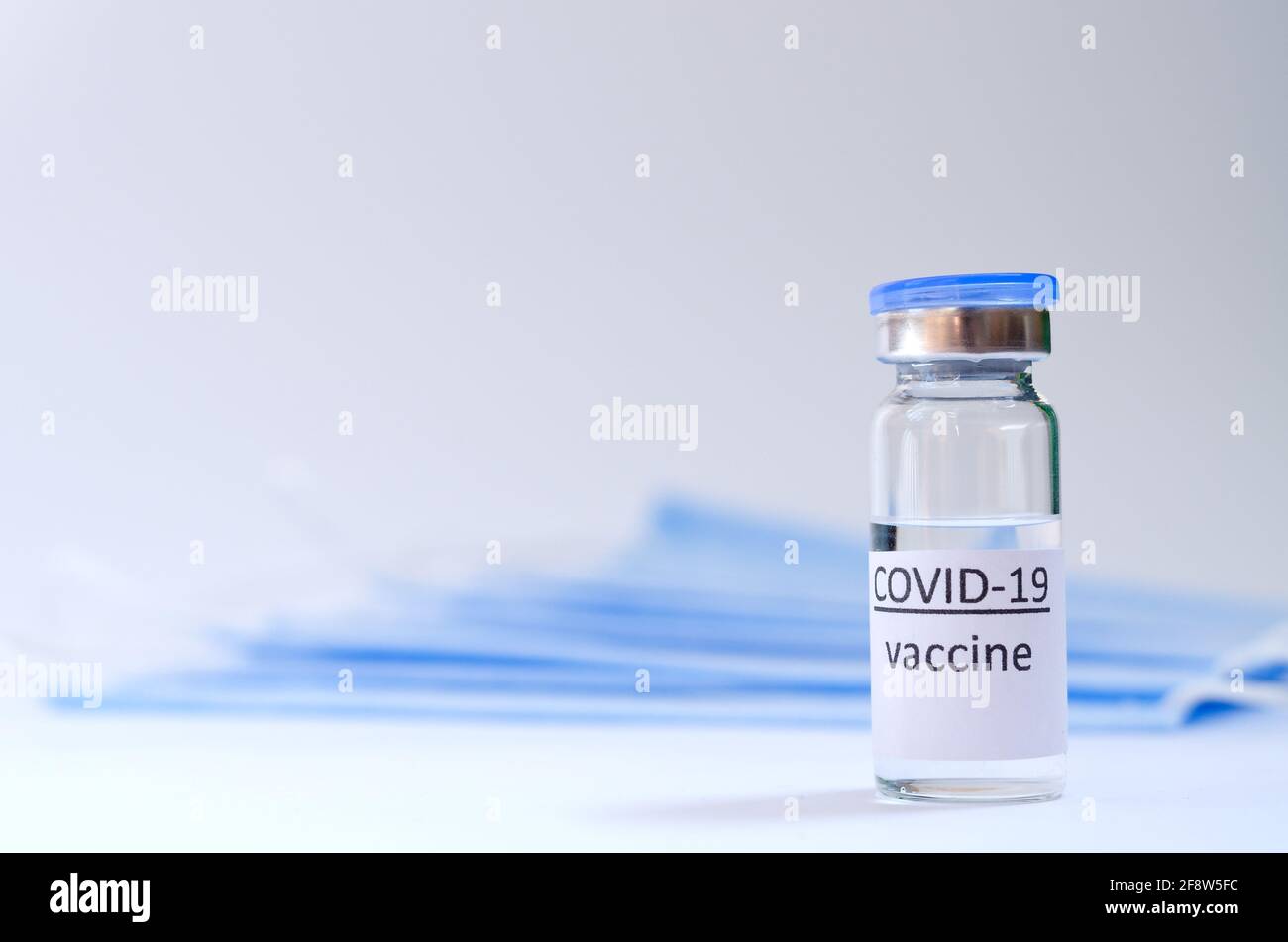 Creative ideas of vaccination concept. Top view of syringe with medical masks and vaccine vial glass bottles for vaccination against COVID-19. Stock Photo