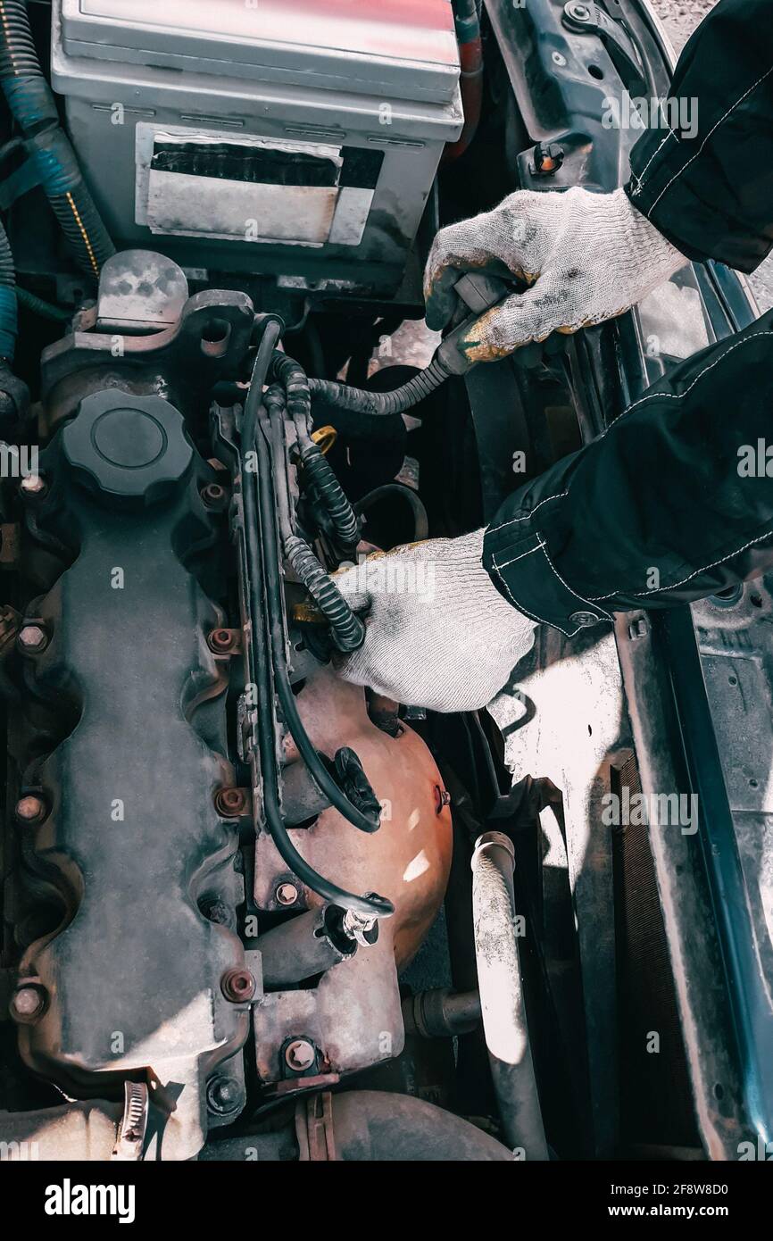 Auto mechanic repairs a car engine. Man's hands in work gloves close-up. Diagnostics and restoration of old parts. Replacement of high-voltage wires. Stock Photo