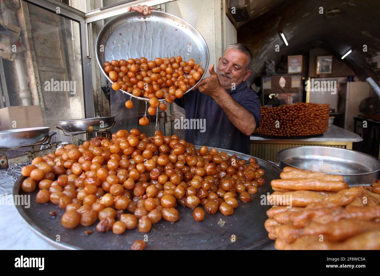 Nablus, Ramadan at a local market in the West Bank city of Nablus. 15th Apr, 2021. A Palestinian vendor makes Luqmat al-Qadi sweets, a traditional pastry made of leavened and deep fried dough, on the third day of Ramadan at a local market in the West Bank city of Nablus, April 15, 2021. Credit: Nidal Eshtayeh/Xinhua/Alamy Live News Stock Photo