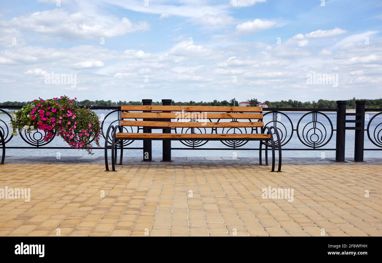 Embankment with bench with view on sea. Park wooden bench on the cobbled sidewalk Stock Photo