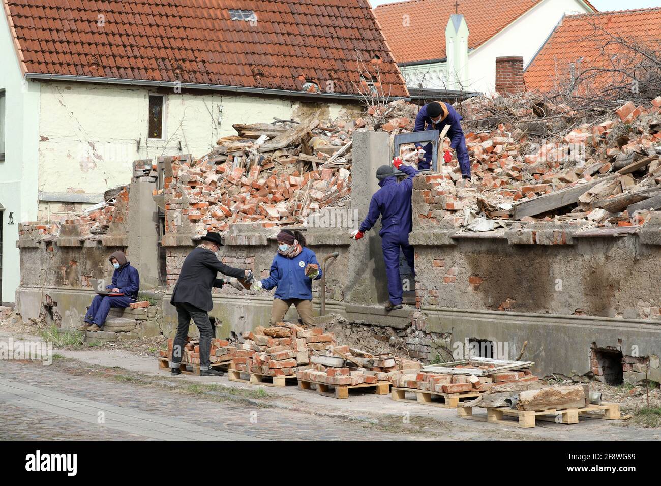 Tribsees, Germany. 15th Apr, 2021. Anna Weberberger (l-r), Ton Matton, initiator and urban planner, Sofie Wagner, project manager, Chaz Gervais and Paulus Goerden from the Art University Linz (Austria) stack bricks and other parts of a demolished house on pallets. The debris will be assembled into an installation at the university that will simulate the atmosphere in the small town. The action is part of the project 'Making Tribsees' Future', which aims to create an atmosphere of departure in the town. Credit: Bernd Wüstneck/dpa-Zentralbild/ZB/dpa/Alamy Live News Stock Photo