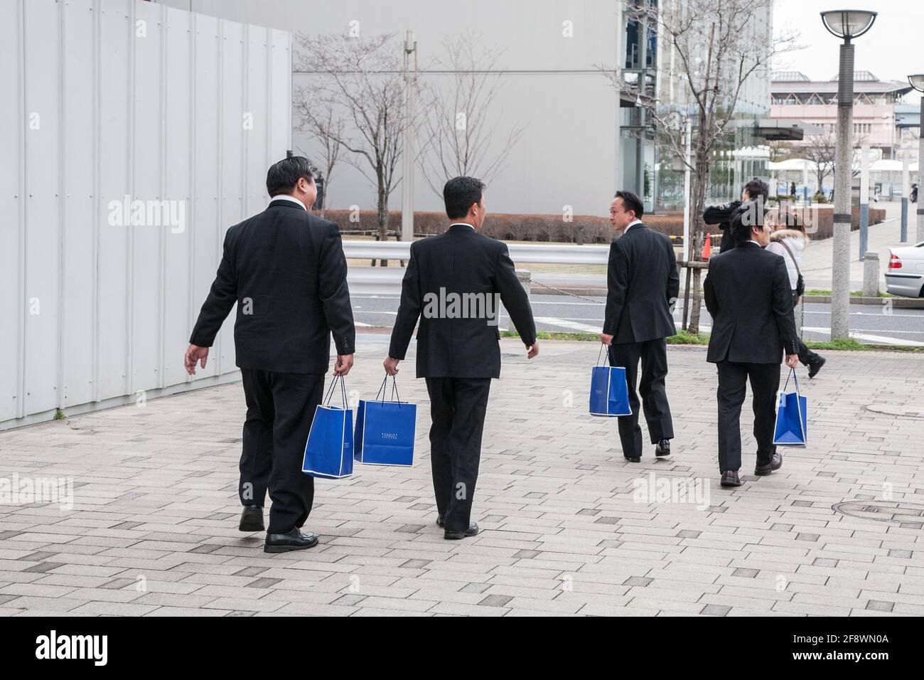Four Japanese men wearing business suits walk on pavement carrying