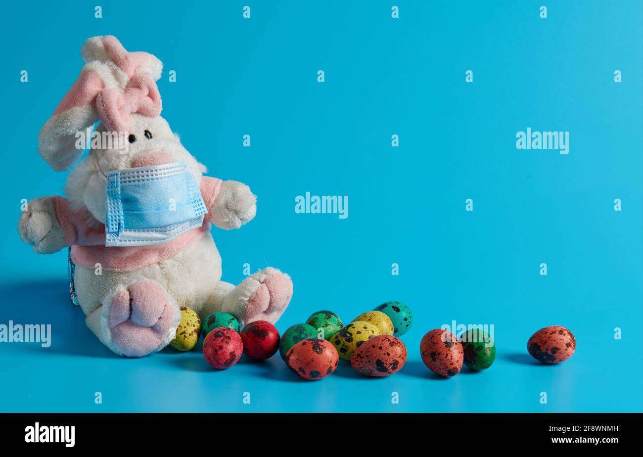 on a blue background white hare in a mask and Easter eggs Stock Photo