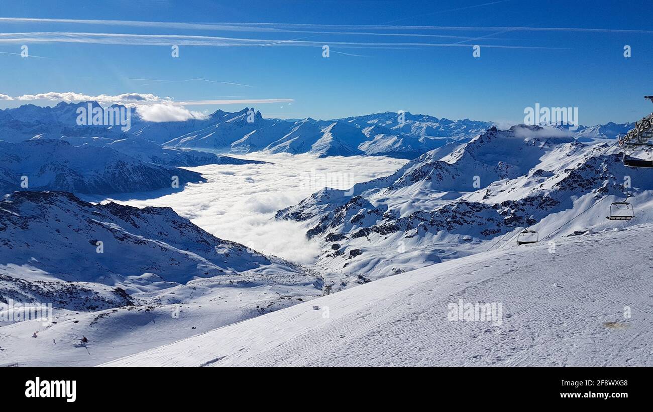 View of the snow-covered peaks of the French Alps, above a cloud cover with a sunny blue sky from the ski area Les Trois Vallees Stock Photo