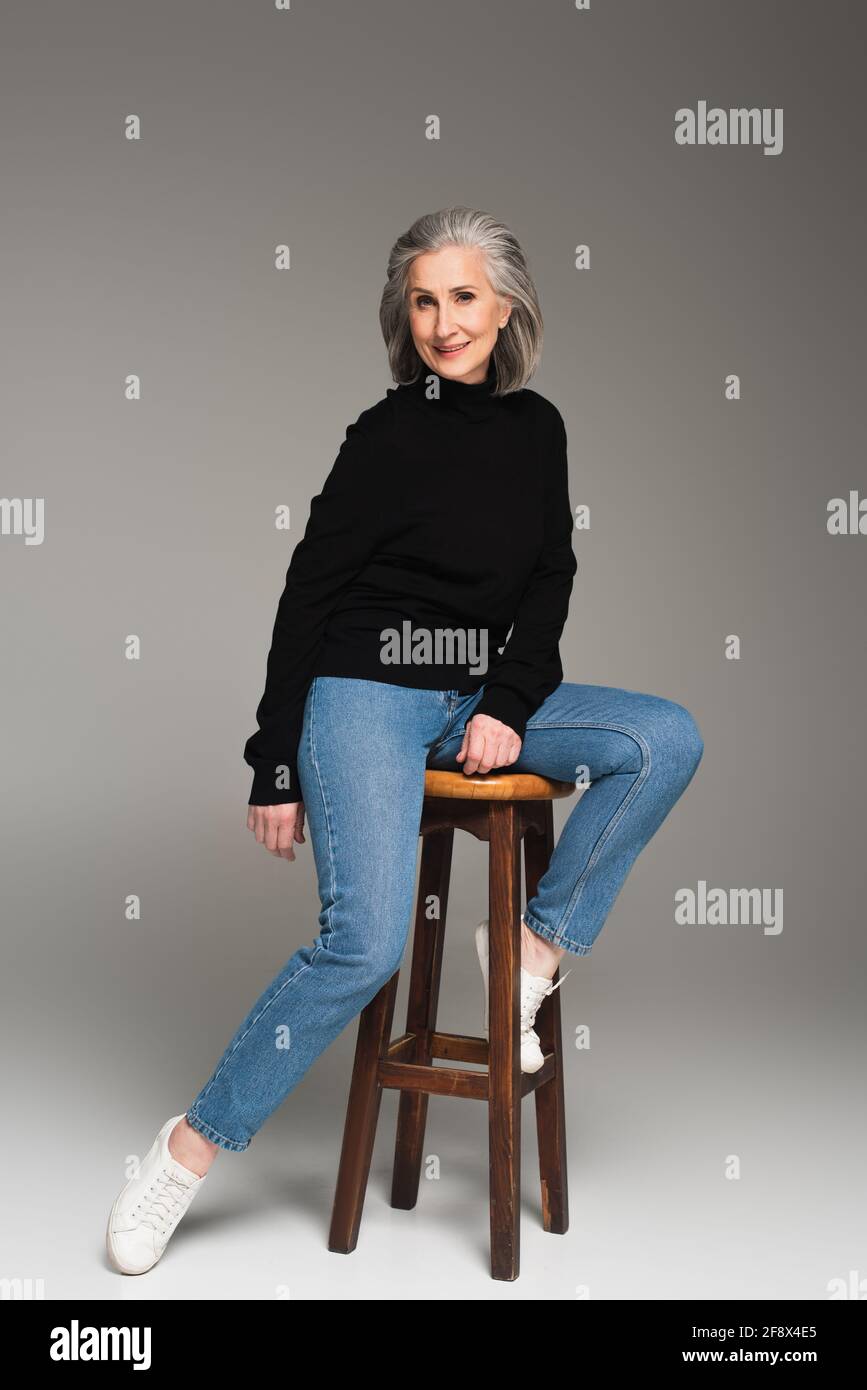 Mature woman sitting on chair and smiling on grey background Stock ...