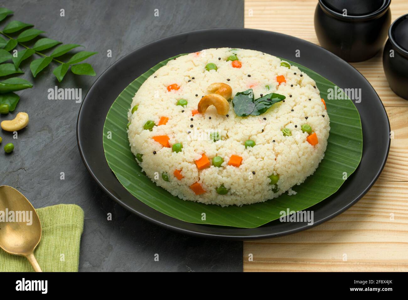 Upma made of samolina or rava upma, most famous south indian breakfast item which is arranged in a  black plate  and garnished with fried cashew nut a Stock Photo