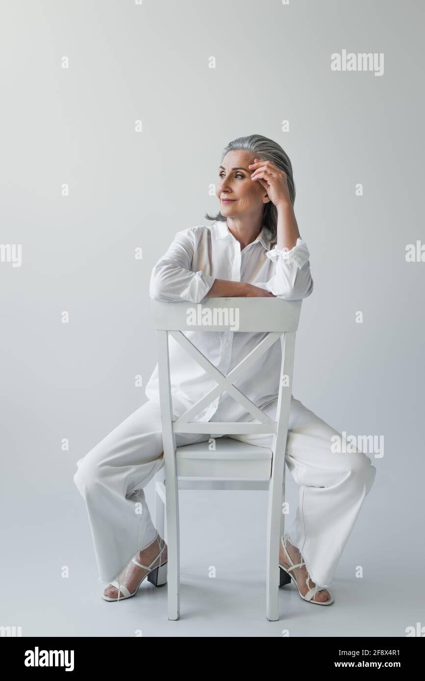 Middle aged woman sitting on chair on grey background Stock Photo - Alamy