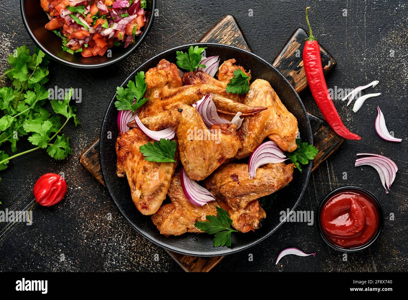 Grilled chicken wings or roasted bbq with spices and tomato salsa sauce on a black plate. Top view with copy space. Stock Photo