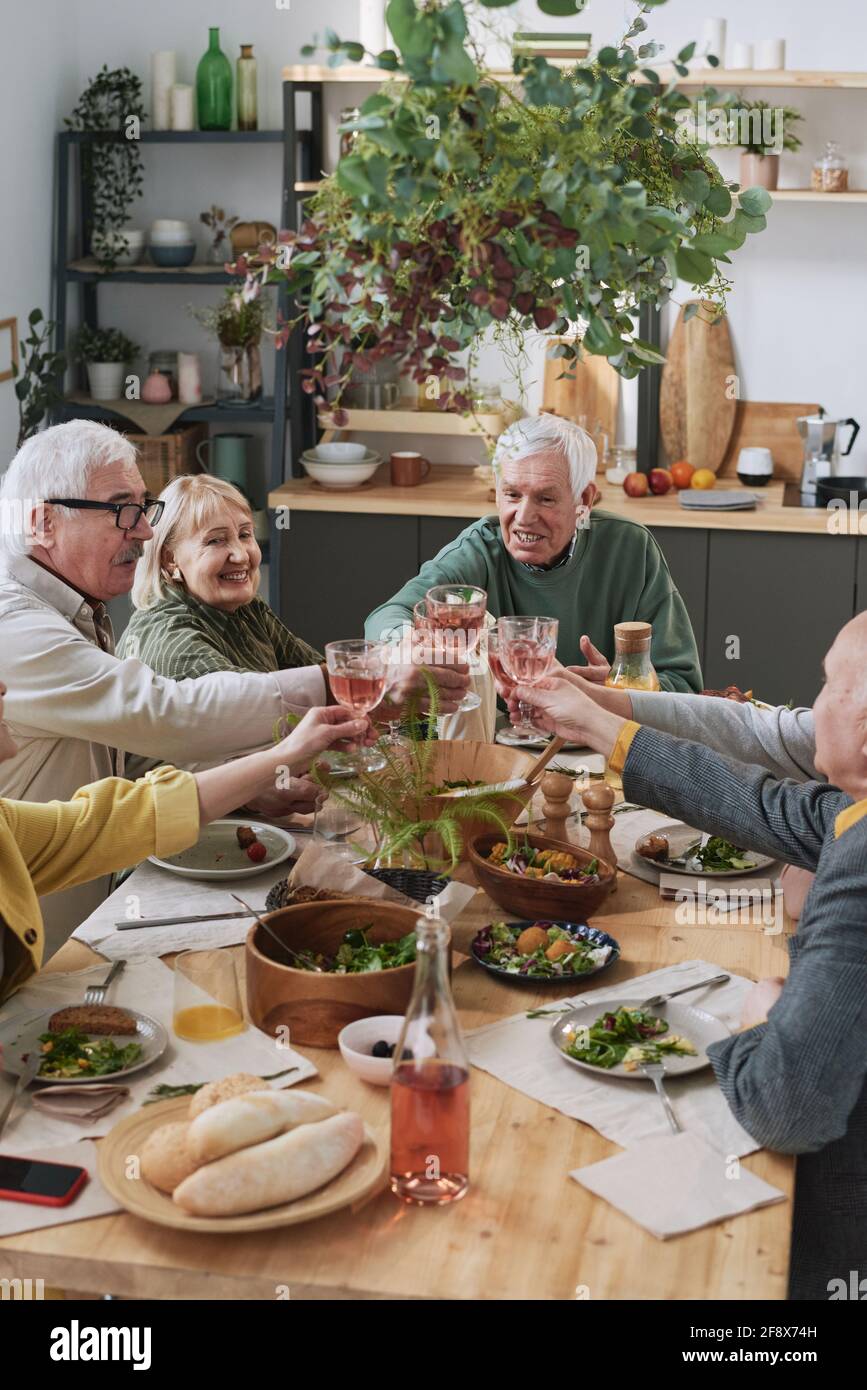Senior friends sitting at the table and raising glasses of red wine during dinner at home Stock Photo