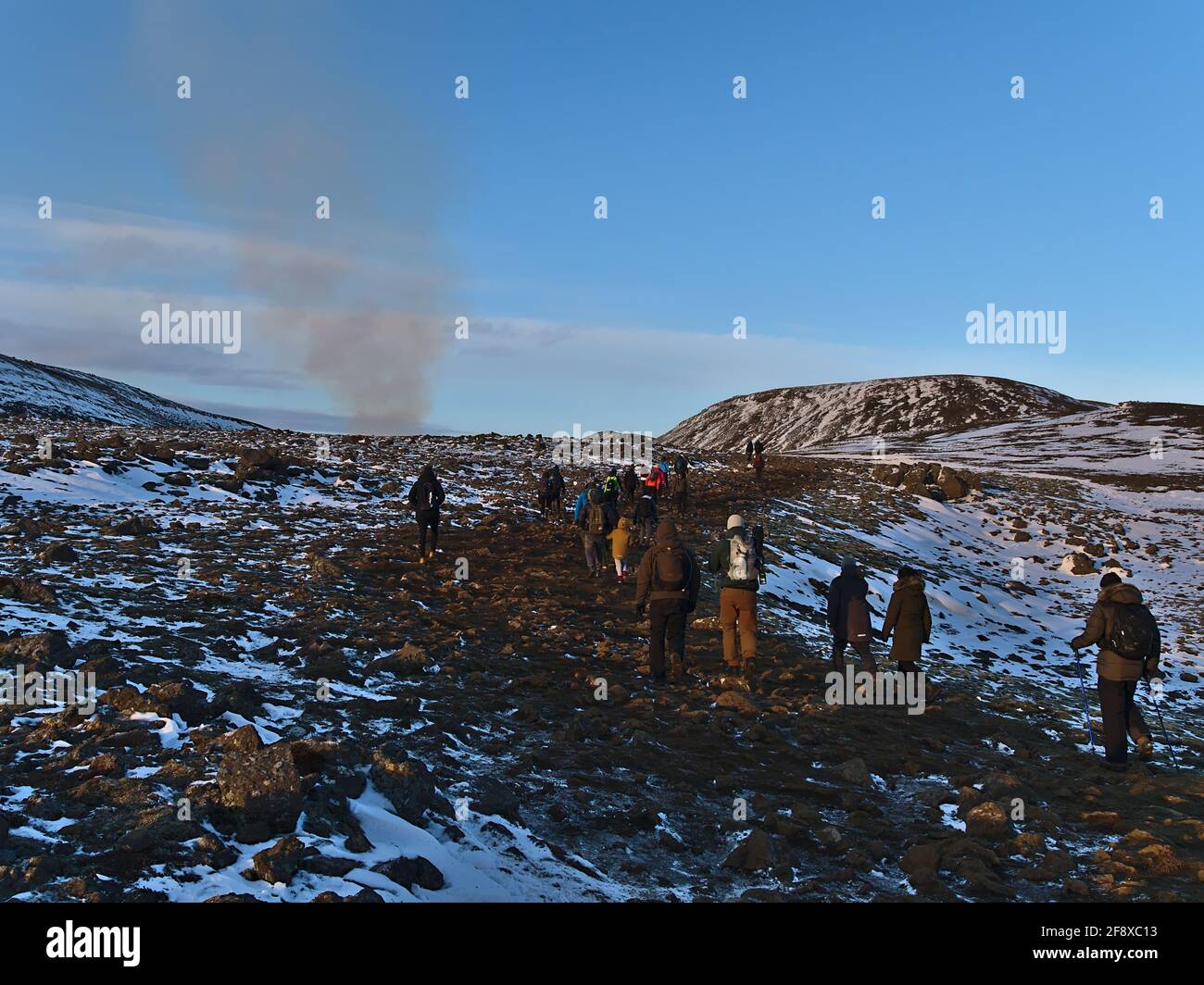 Group of people hiking to recently started volcanic eruption at Fagradalsfjall in Geldingadalir valleys with smoke of the volcano on sunny winter day. Stock Photo