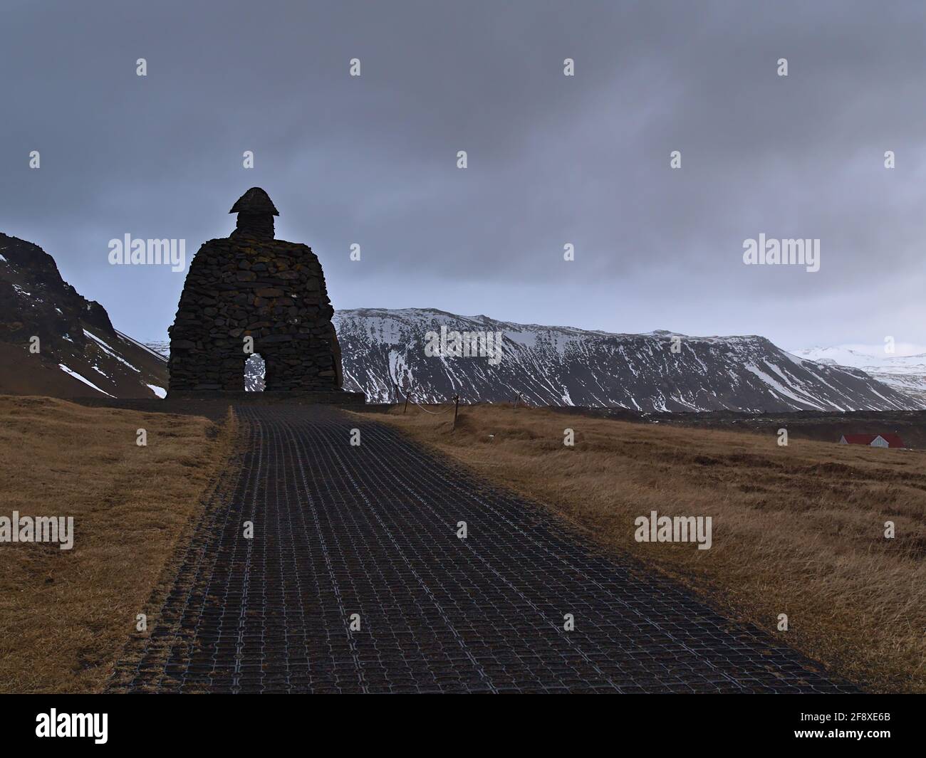 View of a big statue made of volcanic rocks  with relation to the Bárðar saga Snæfellsáss in small village Arnarstapi in winter with mountains. Stock Photo