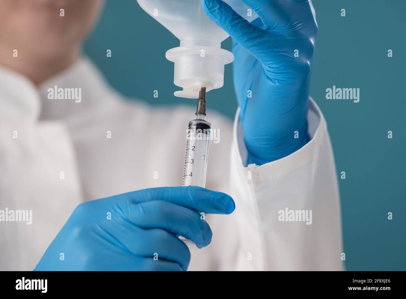 Close-up of a syringe set of a transparent drug from a vial on a blue background. Stock Photo