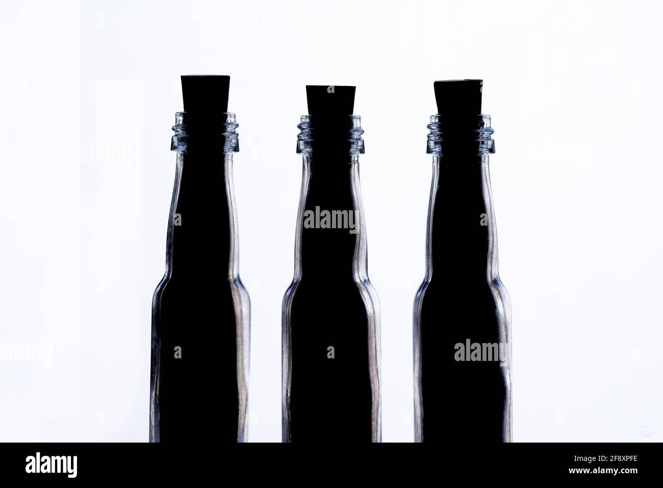 Three-quarters shot of three small backlit glass bottles in a row. Flacons are filled with content to the top and sealed with cork stoppers. Stock Photo