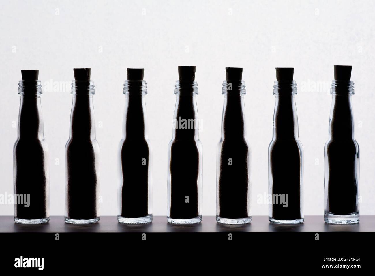 Seven small backlit glass bottles in a row, on white background. Flacons are filled with content to the top and sealed with cork stoppers. Stock Photo