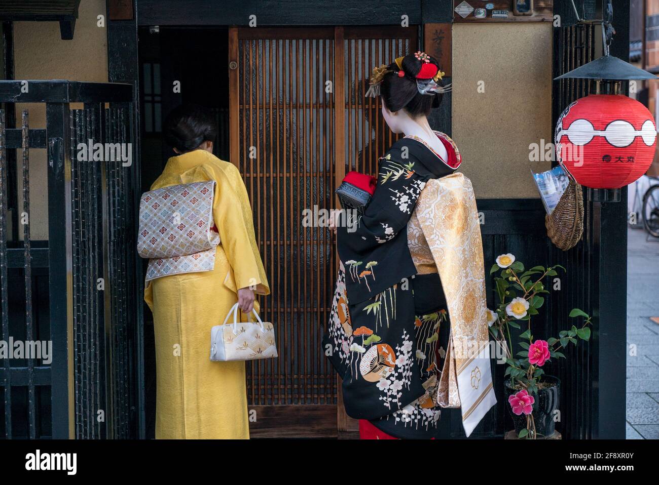 Japanese Geisha Maiko. Performer and chaperone calling at door of a client. Wearing traditional kimono dress and white make-up. Gion, Kyoto, Japan Stock Photo