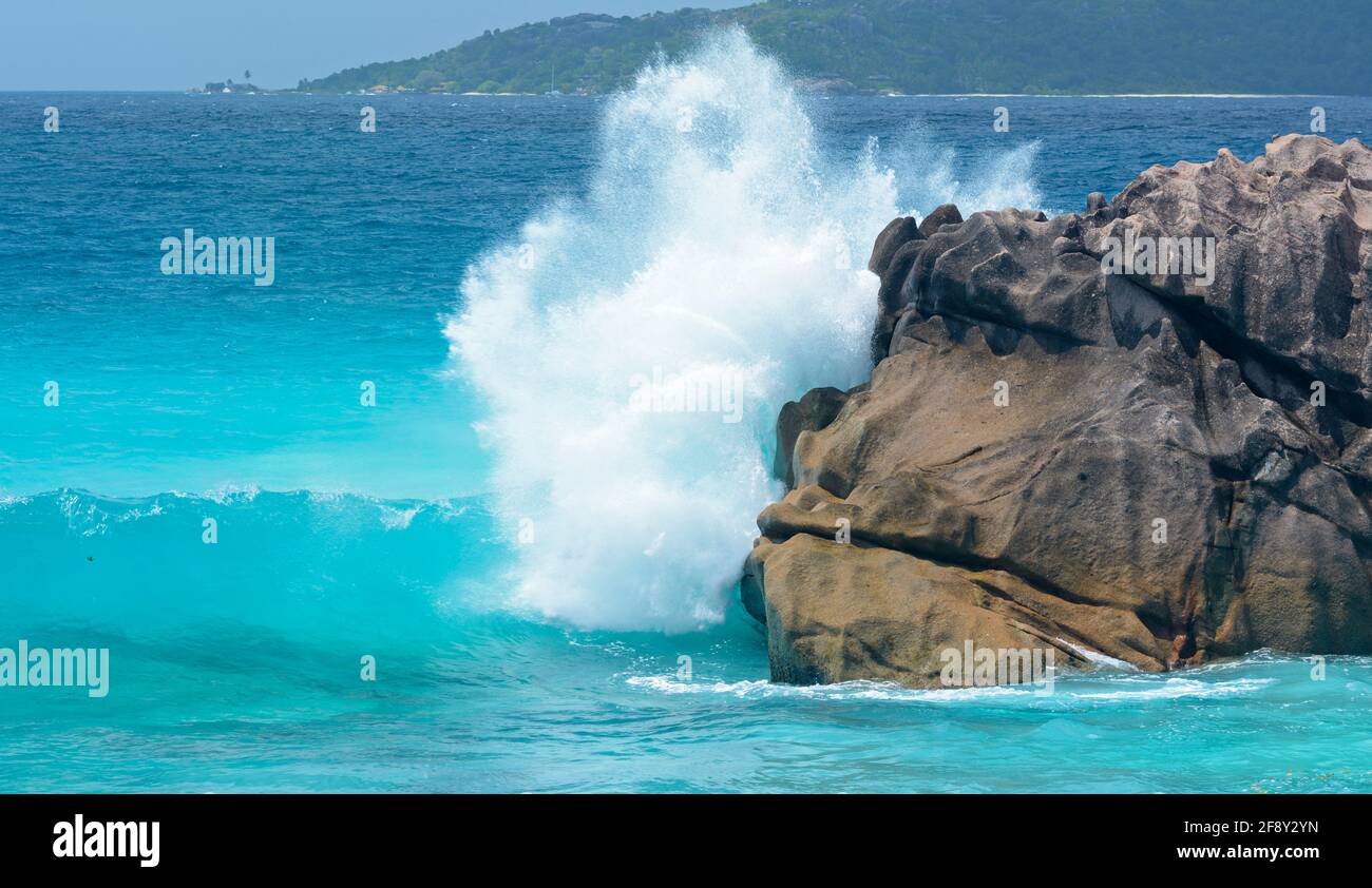Sea wave splashing on offshore boulder, Anse Patates, Seychelles Stock Photo