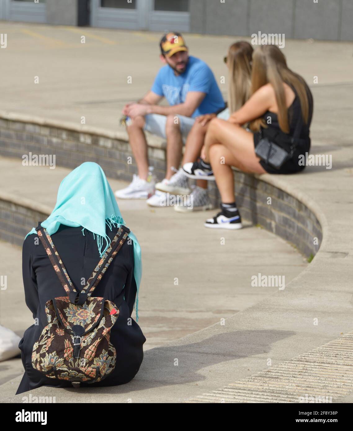 Muslim woman in black with hijab, facing 3 people in shorts & vests Stock Photo