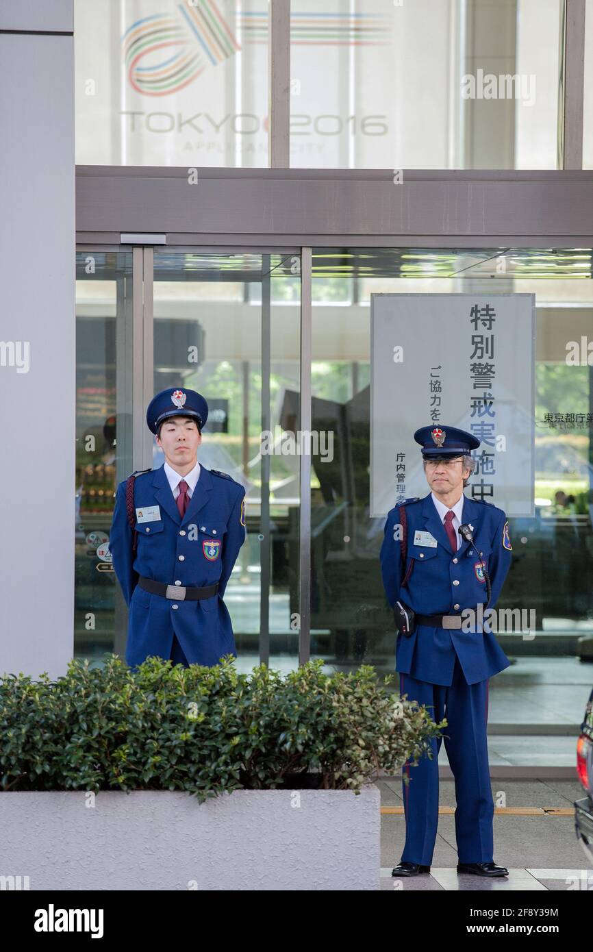 Two Japanese security guards stand outside building below graphic for