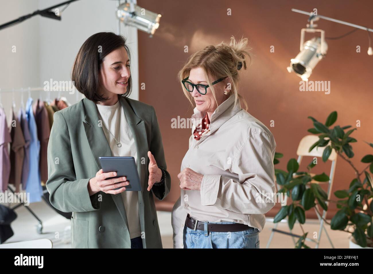 Two fashion designers discussing new collection and using digital tablet while standing at studio Stock Photo