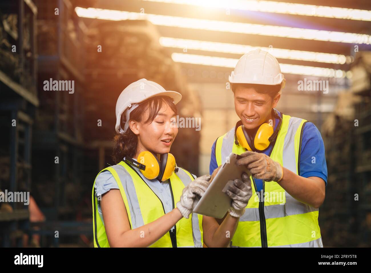 Asian young man and women worker team engineer working help support together using tablet happy smile to work in factory industry Stock Photo