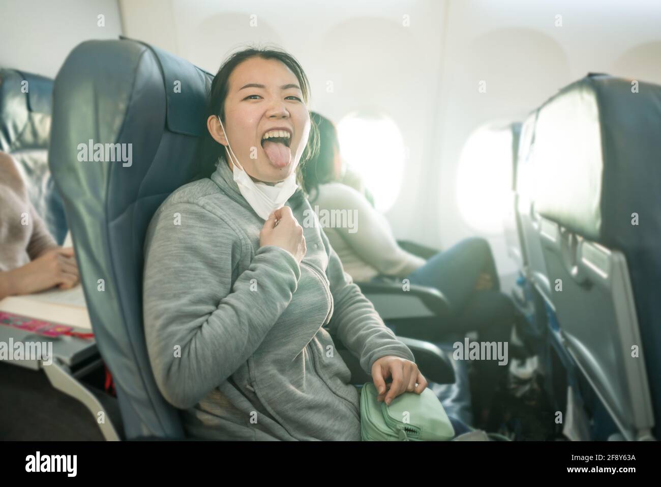 Asian tourist woman flying in times of covid19 - young happy and funny  Korean girl pulling off mask breathing free on airplane cabin ready for  flight Stock Photo - Alamy