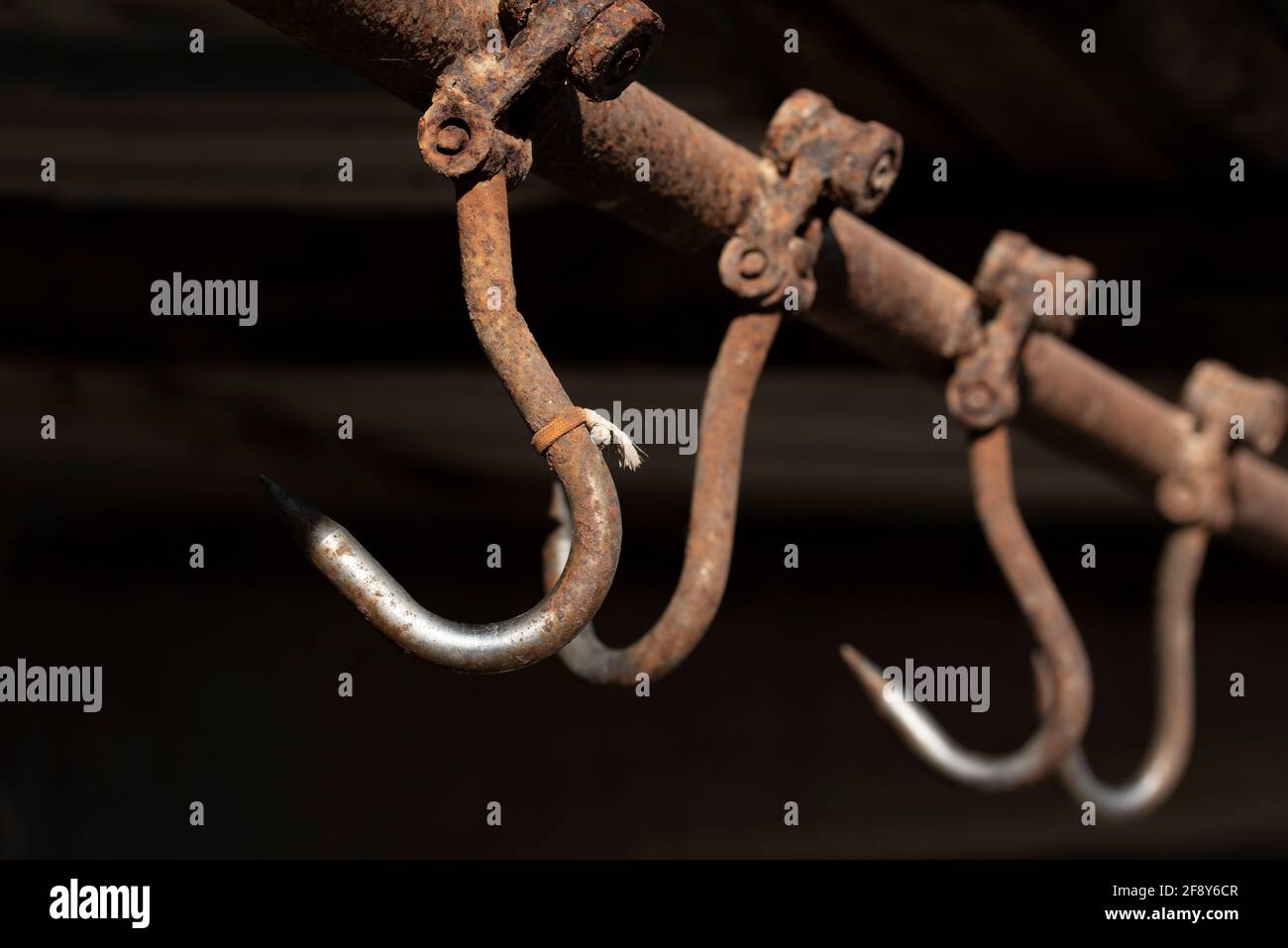 Rusty meat hooks hang from the ceiling against a dark background Stock Photo