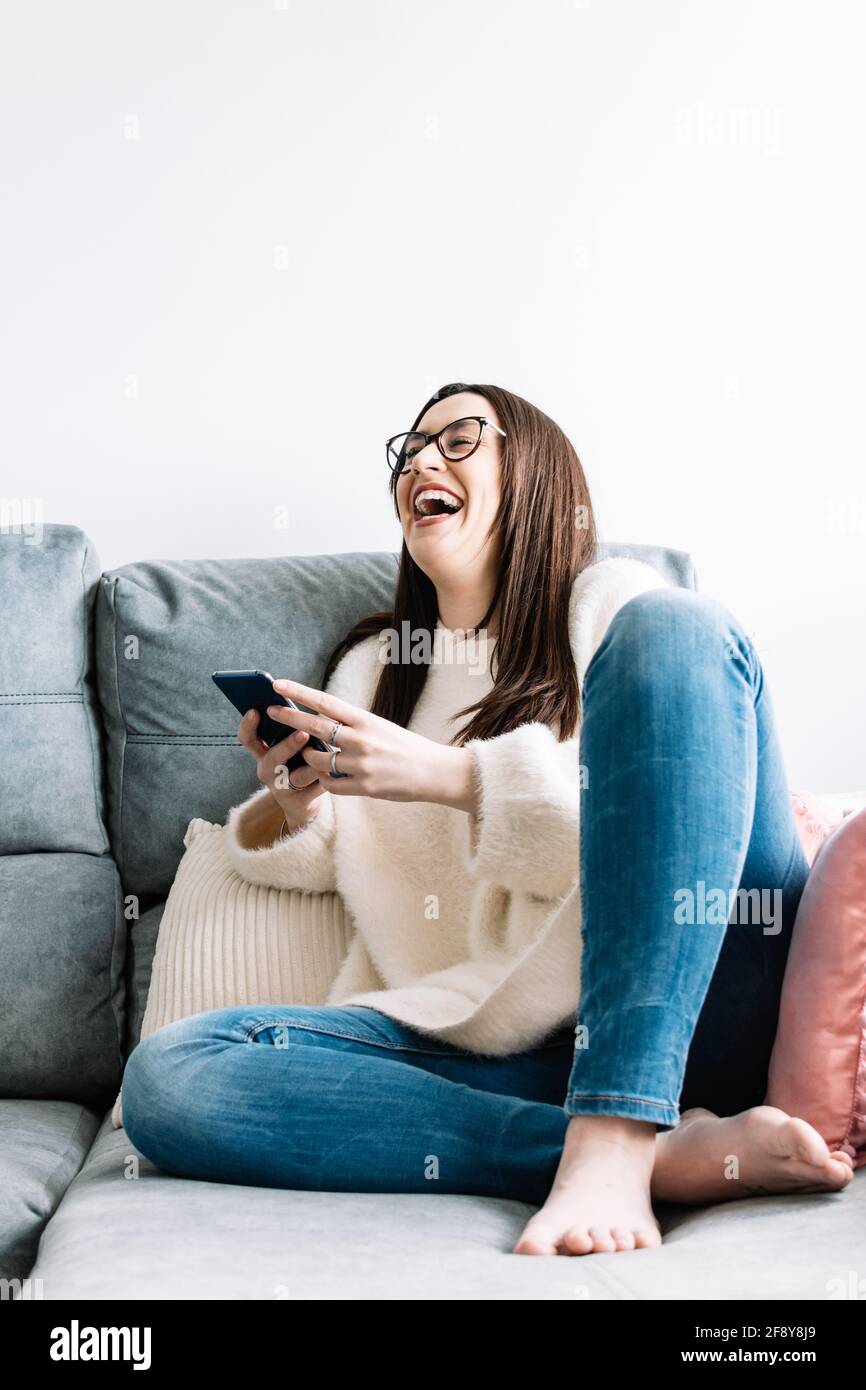 woman using mobile phone while sitting on a couch at home. Stock Photo