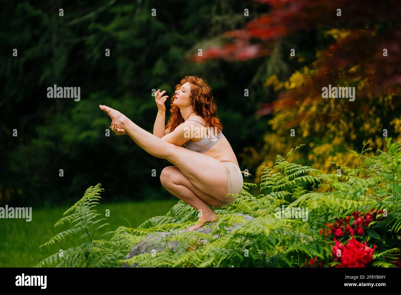 Redhead woman doing yoga on stone in forest Stock Photo