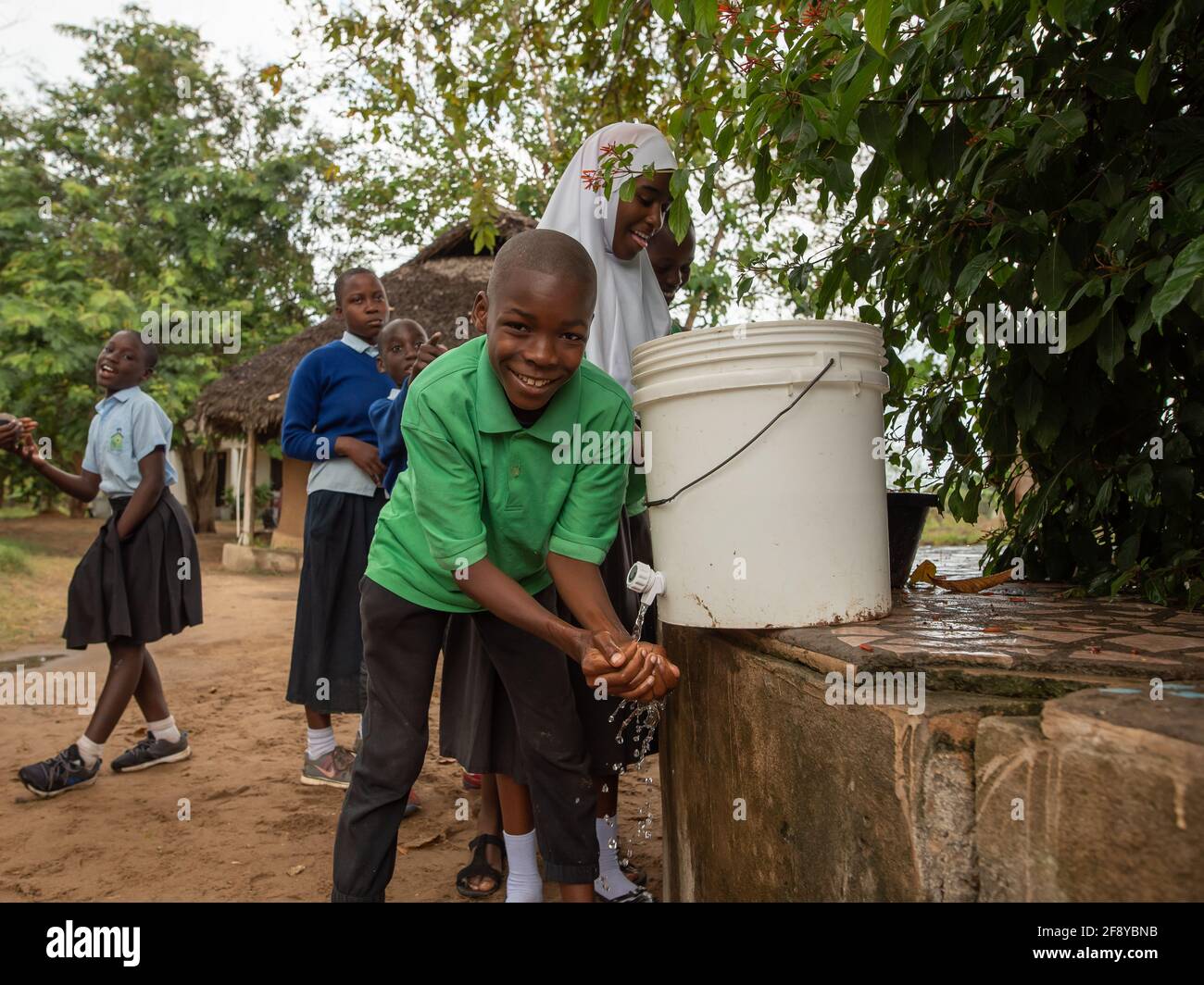 Dodoma, Tanzania. 08-18-2019. A male black muslim boy finishes lunch in their school and is making a line to wash his hands after lunch in a remote vi Stock Photo