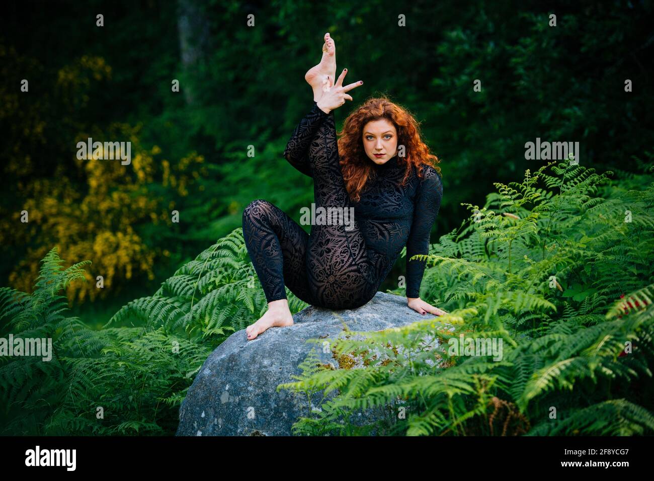 Redhead woman doing yoga on stone in forest Stock Photo