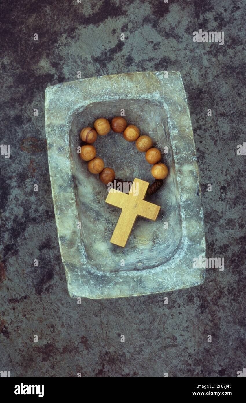 Small marble dish containing wooden cross attached to small band of prayer beads Stock Photo
