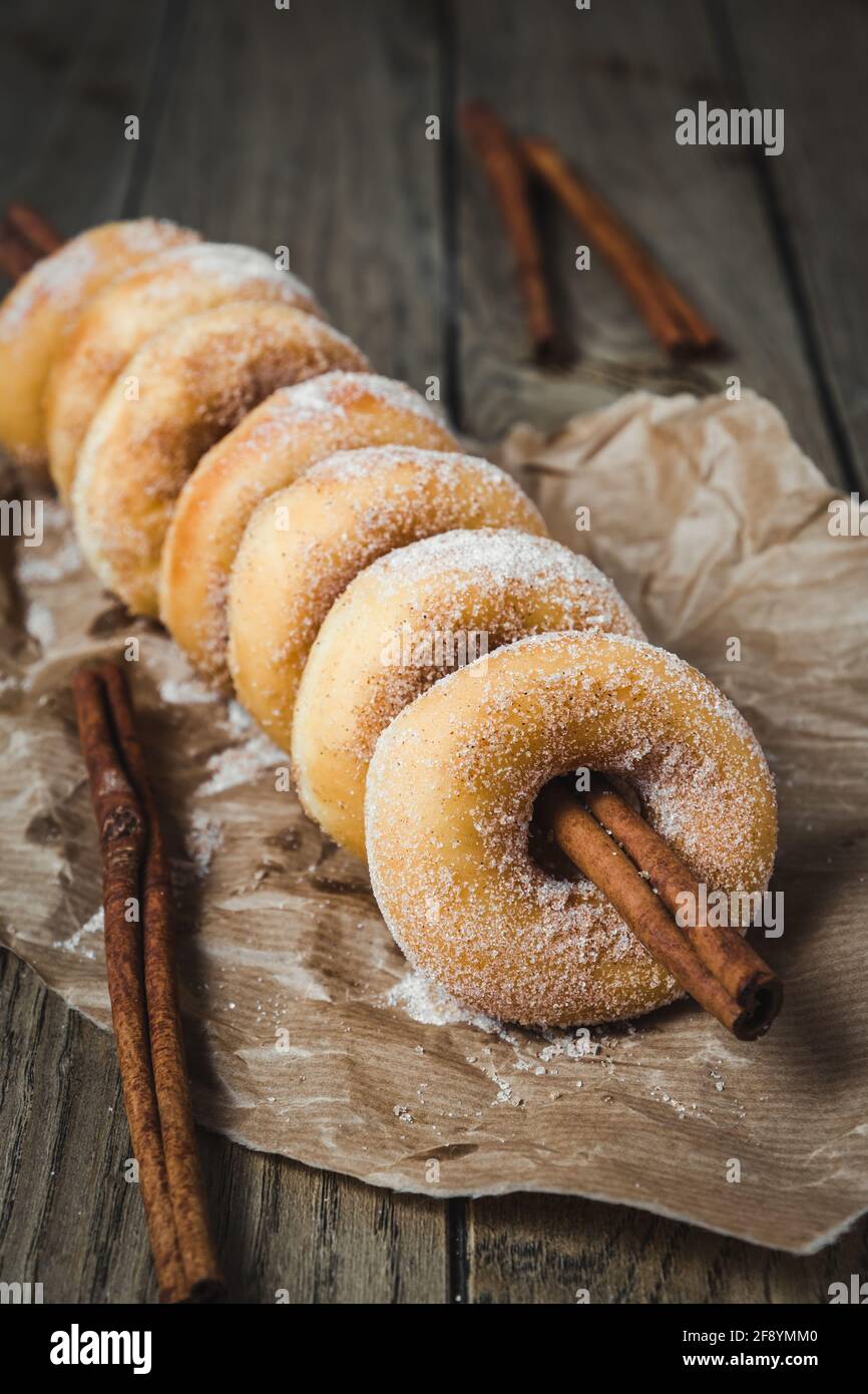 Sugared mini donuts lined up on a cinnamon stick on a wooden table, vertical Stock Photo