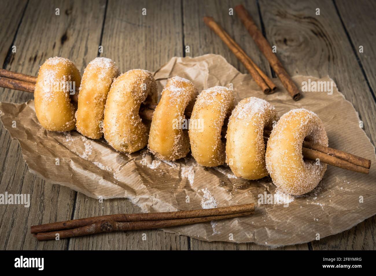 Sugared mini donuts lined up on a cinnamon stick on a wooden table Stock Photo