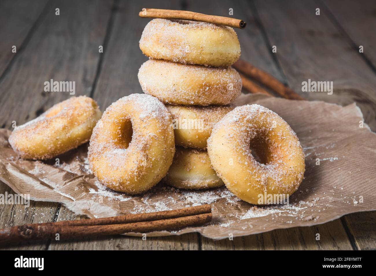 Sugared stacked mini donuts with cinnamon on brown paper on a wooden table Stock Photo