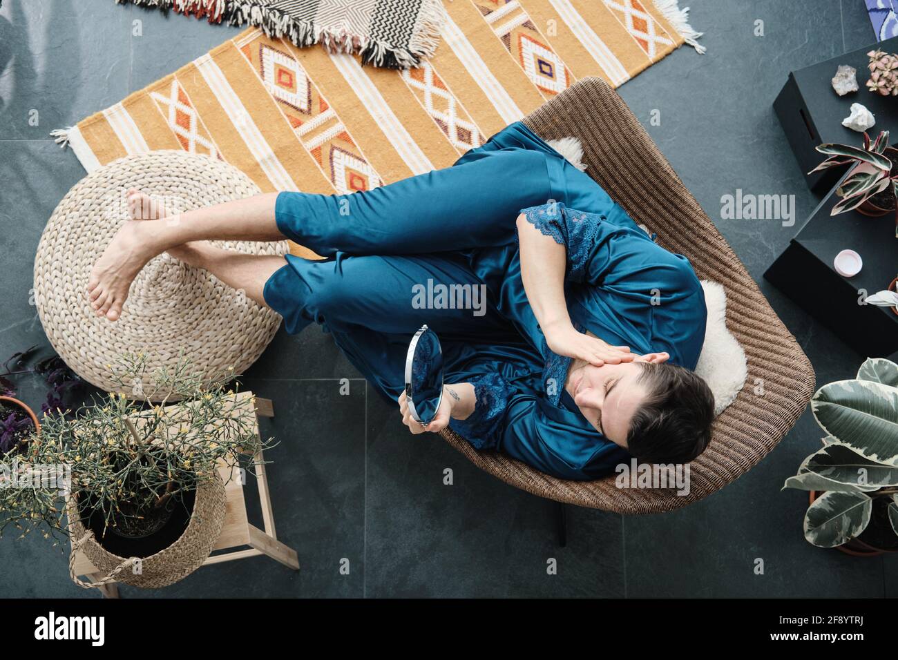 High angle view of young man in female dressing gown sitting on armchair and looking at mirror he caring about his beauty Stock Photo