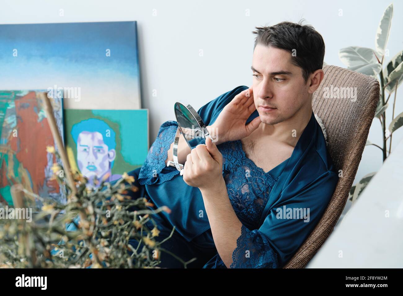 Young transgender sitting in armchair and looking at mirror he applying