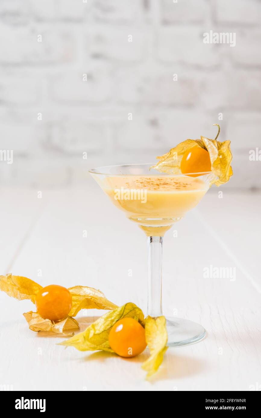 Glass with eggnogg and physalis fruits on white background, vertical with copy space Stock Photo