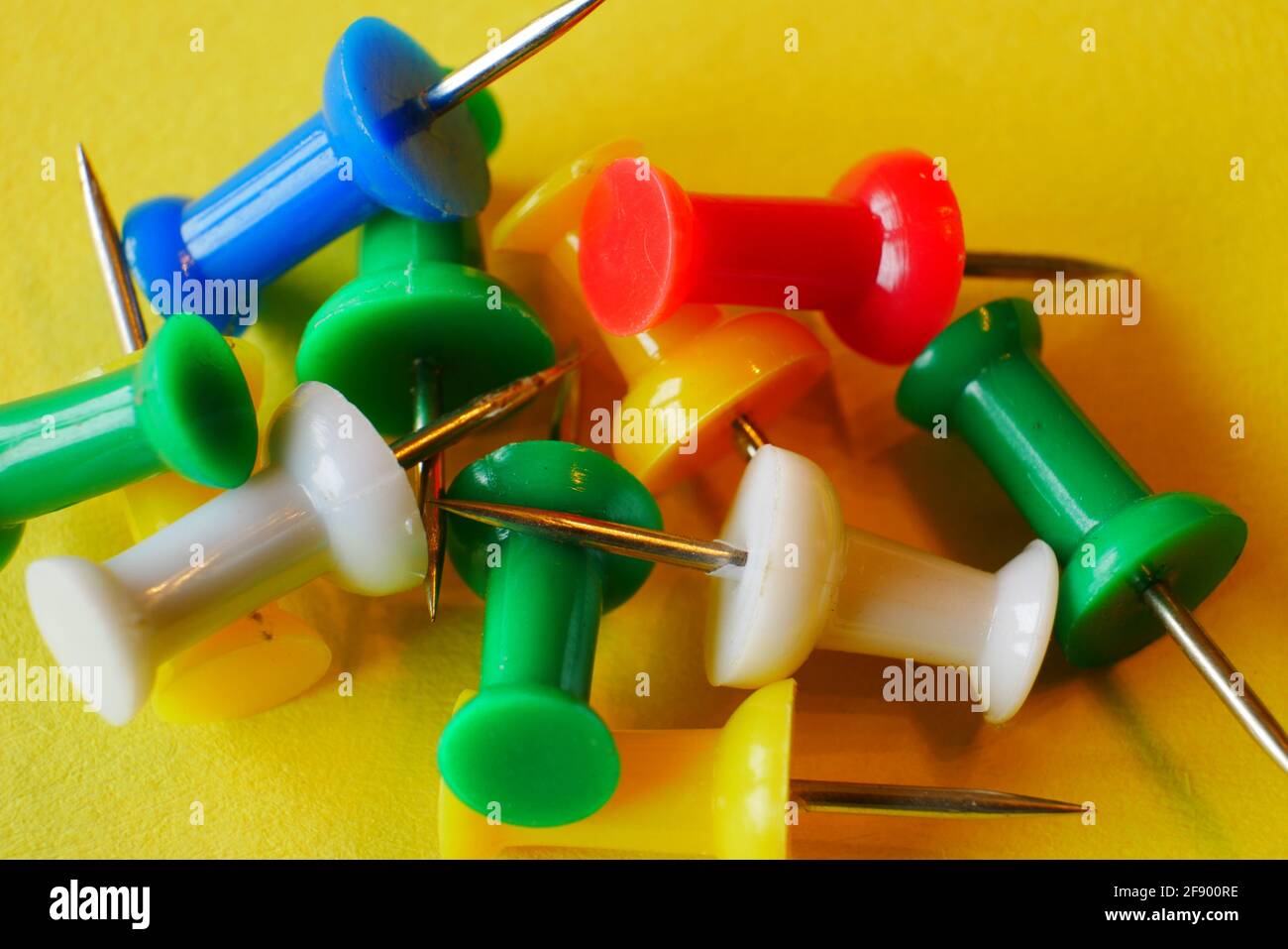 close up of colorful thumbtacks in the colors red yellow white blue green on yellow paper Stock Photo