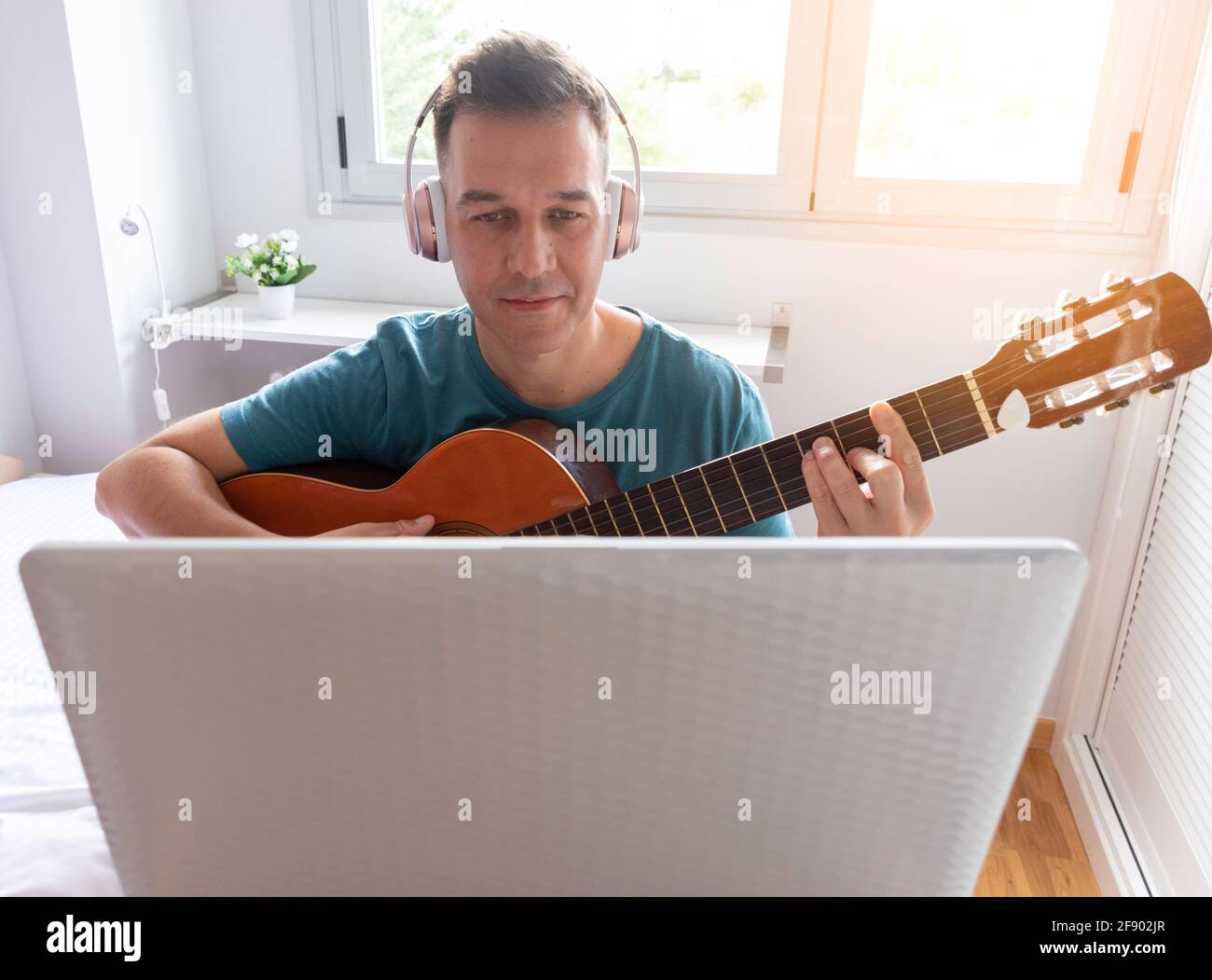 Caucasian man checks his laptop while learning to play guitar online Stock Photo