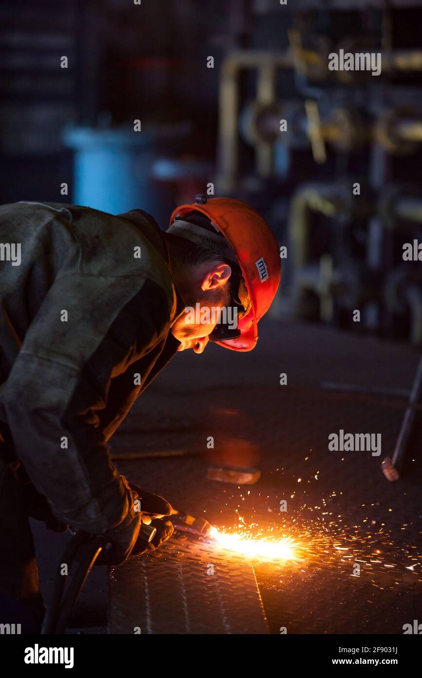 Aksu, Pavlodar region, Kazakhstan: Aksu steam power station. Welder worker in orange hardhat welding metal grid floor. Stock Photo