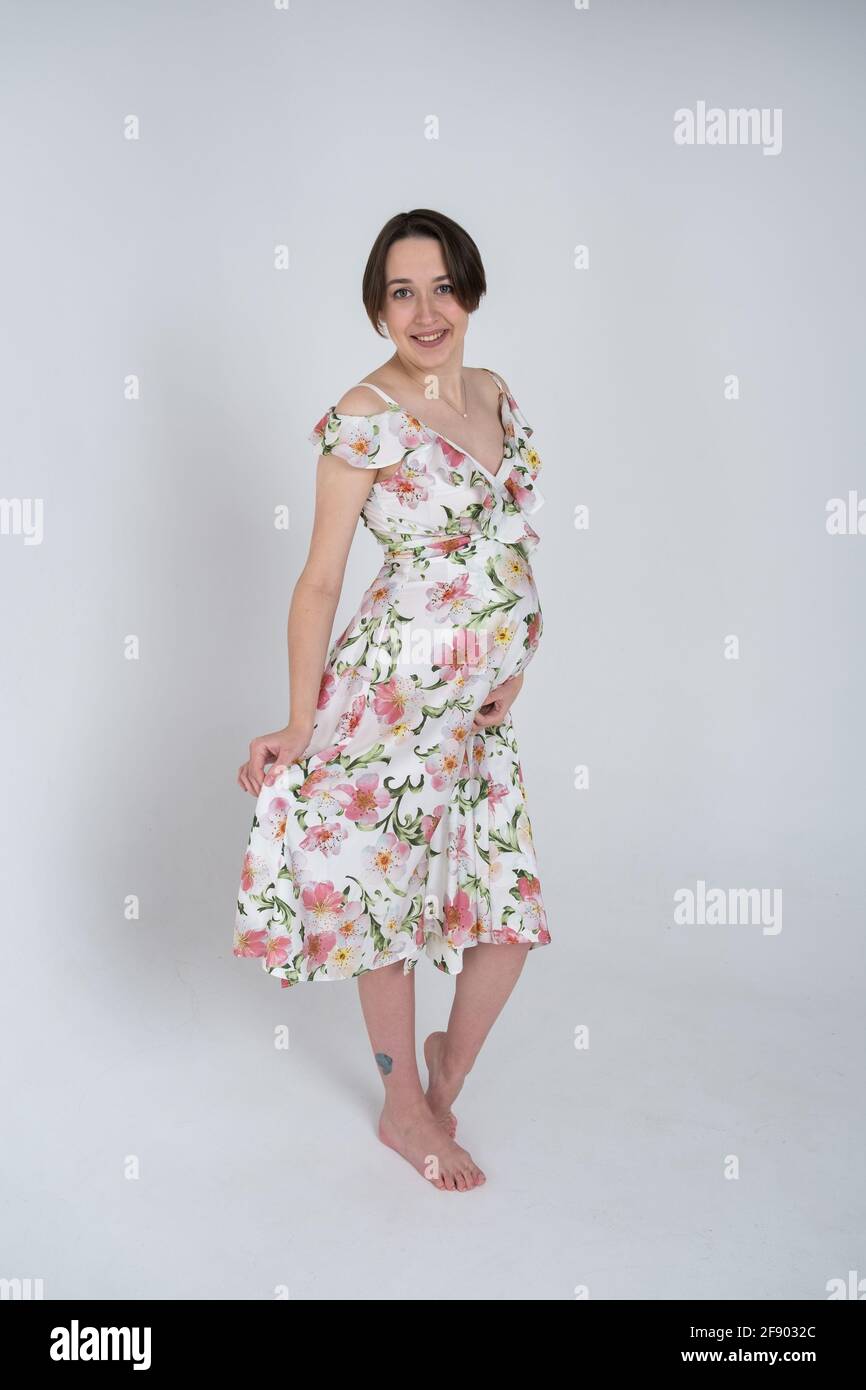 Studio portrait of cheerful young pregnant woman in summer dress on white gray background, happy pregnancy concept Stock Photo