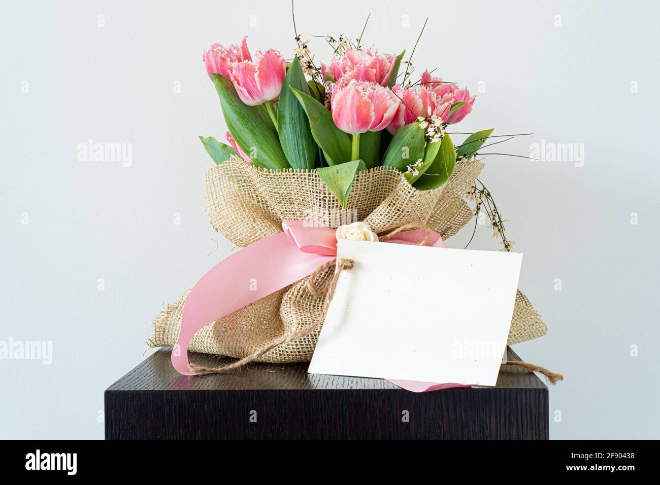 Blank paper greeting card, invitation. Bouquet of fresh pink tulips wrapped in burlap fabric (jute). Elegant wooden perch of interior design. Wedding, Stock Photo